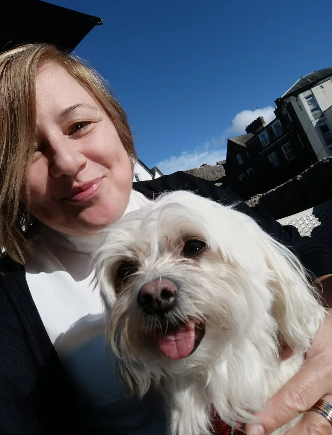 Liz cuddling a small white dog outdoors